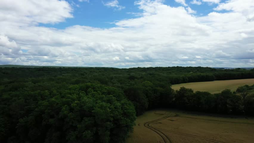 Aerial view of lush green forest and open fields under a partly cloudy sky in the French countryside. Peaceful rural scenery with natural greenery and farmland.