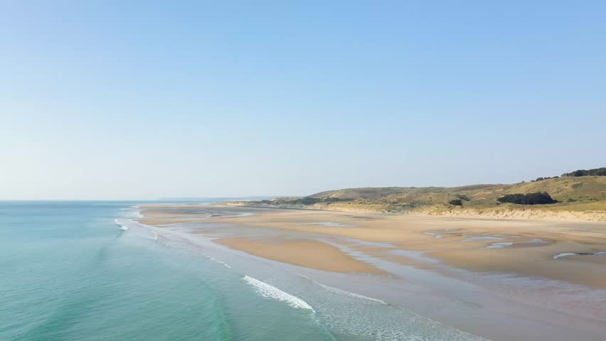Aerial view of the expansive sandy shoreline and gentle waves at Plage de la Vieille eglise under a clear blue sky.