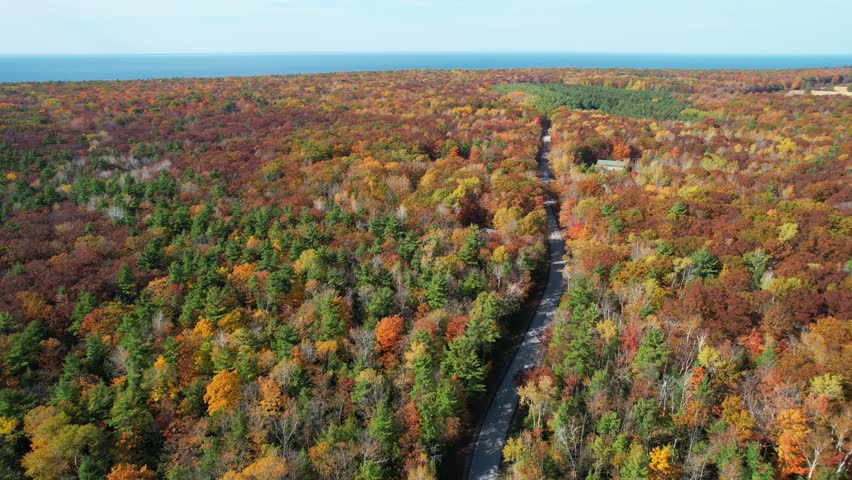 Aerial view of Door County Wisconsin Country roads in Autumn.  Dramatic view of black car driving on warm fall sunny day. Wide and high drone shot of car with Lake Michigan on the Horizon.