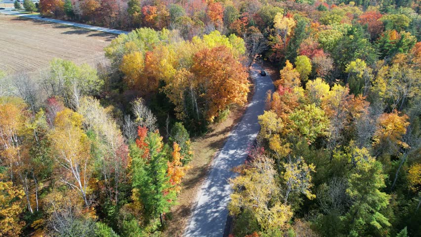 Aerial view of Door County Wisconsin Country roads in Autumn.  Dramatic view of black car driving on warm fall sunny day.  Drone follow shot.
