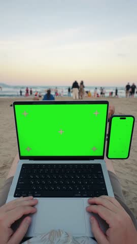 
POV working on laptop and smartphone with green screens on beach