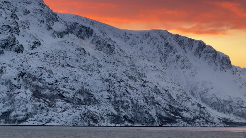 Sunset over snowy mountains near the water in Norway during winter months