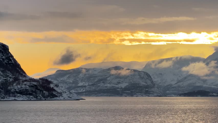 Sunset over snowy mountains near the water in Norway during winter months