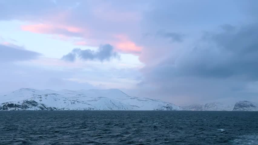 Sunset over snowy mountains near the water in Norway during winter months