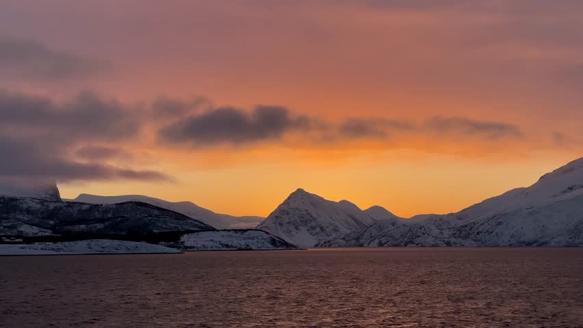 Sunset over snowy mountains near the water in Norway during winter months