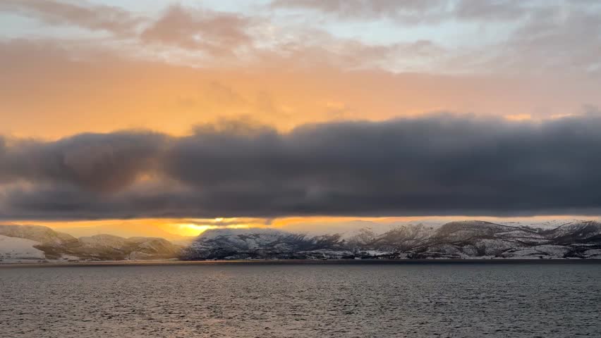 Sunset over snowy mountains near the water in Norway during winter months