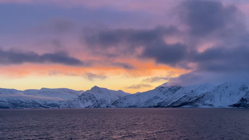 Sunset over snowy mountains near the water in Norway during winter months
