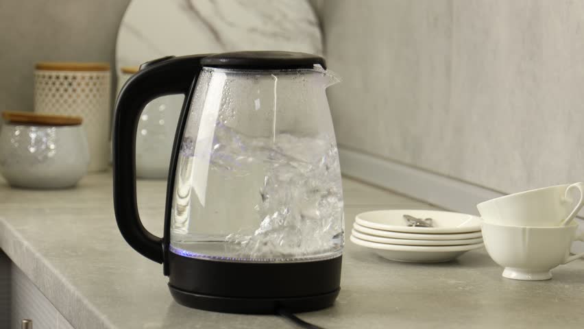 Water boiling in electric kettle and woman taking cup to make tea in kitchen, closeup