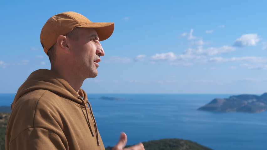 Man using asthma inhaler outdoors overlooking the sea. Man in a cap experiencing an asthma attack and using an inhaler for relief while standing on a mountain with a stunning sea view