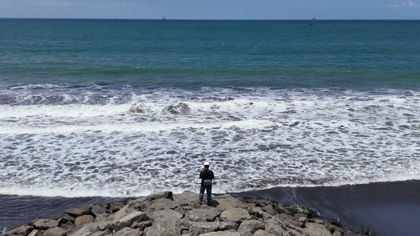A man stands at the end of the stairs facing the sea