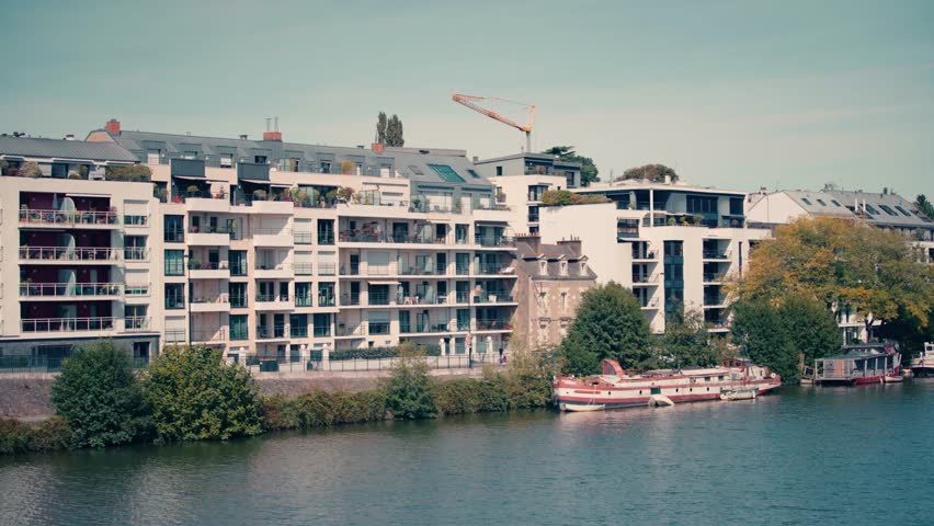 Residential buildings and modern architecture facing the Erdre river in Nantes with a red boat docked at the quay. Wide view of urban living environment and riverside housing.