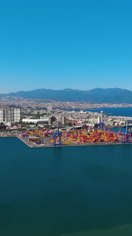 Vertical video. Izmir, Turkey. Aerial view of Izmir Port container terminal with stacking area and large cranes for cargo operations on sunny summer day. Aerial view. Rich colors