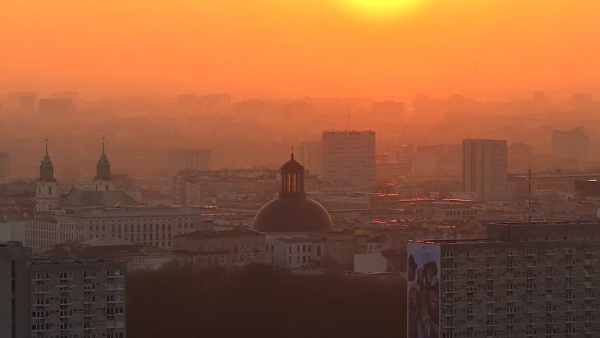 Hazy aerial cityscape of warsaw, poland, during a stunning orange sunrise. The holy trinity lutheran church dome is a prominent landmark