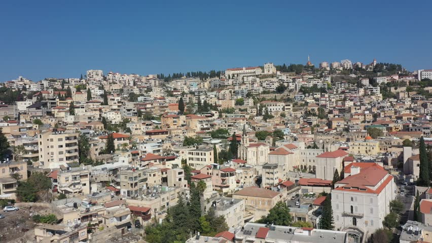 Cinematic aerial drone footage of Nazareth city skyline with dense hillside buildings and historic churches in northern Israel. Scenic urban landscape and architecture in the Middle East.