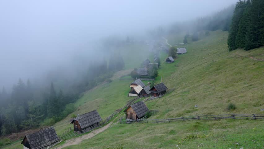 Misty fog moving over a traditional mountain village with wooden huts. Spooky and atmospheric scenery in a rural landscape on a cloudy day