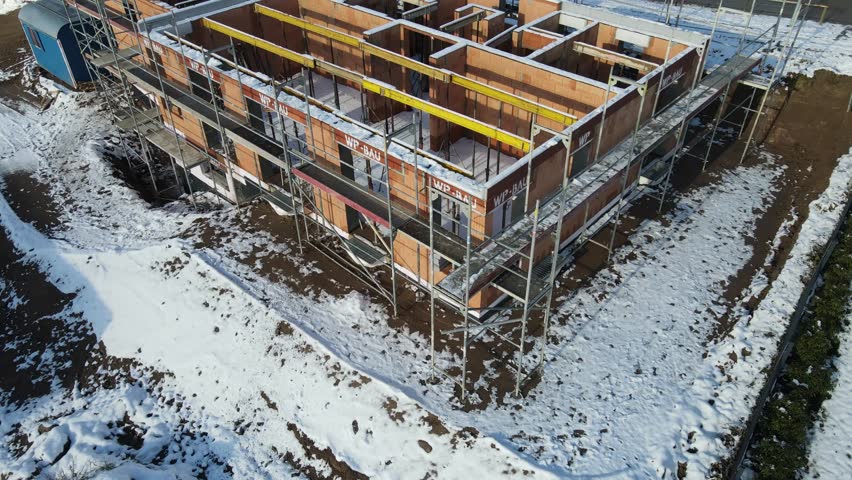 Residential house construction with brick masonry walls and surrounding scaffolding during winter. Modern housing development showing early building phase with exposed masonry at construction site