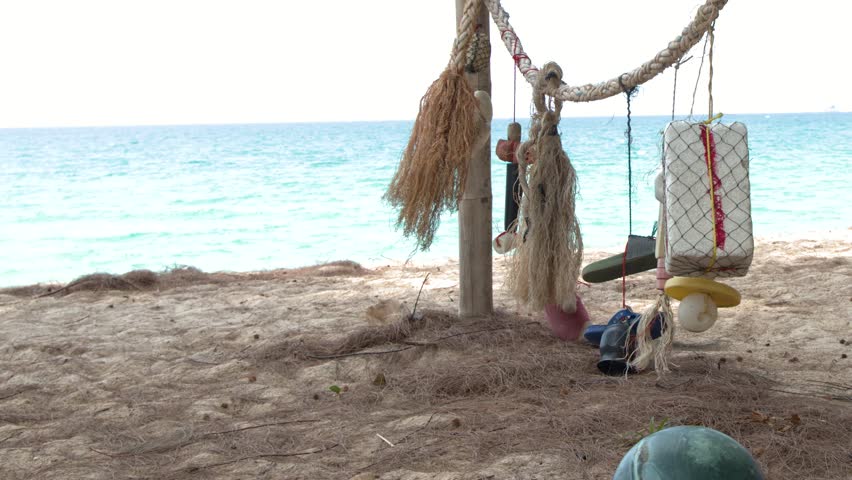 Static shot of fishing floats and ropes hanging on a sandy beach with turquoise water