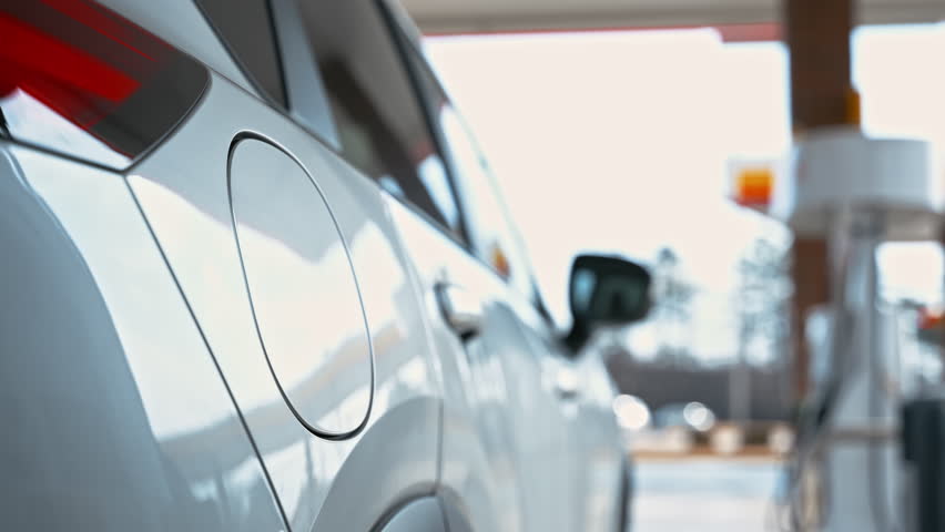 Person refueling a car at gas station using fuel pump nozzle during vehicle fueling.