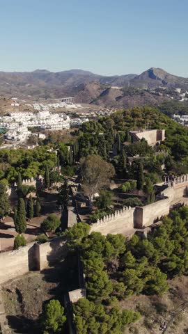 Gibralfaro Castle on its hilltop with sweeping views of Málaga coastline and city below. Vertical Aerial