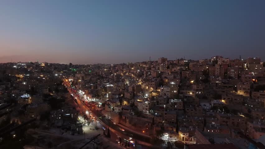Amman cityscape time lapse at dusk turning to night with dense hillside buildings busy road traffic and urban lights Jordan