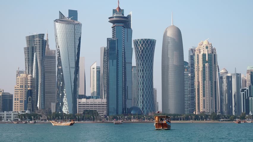 A panoramic view of the impressive skyscrapers and modern architecture of Doha city skyline, with boats navigating the calm waters of the Persian Gulf