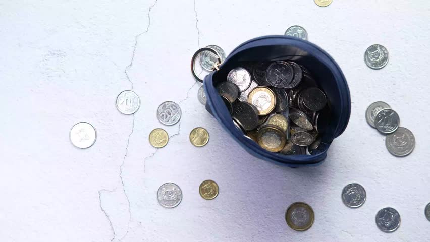 Coins dropping into small blue pouch and scattering on white textured surface, showcasing savings and investment concepts