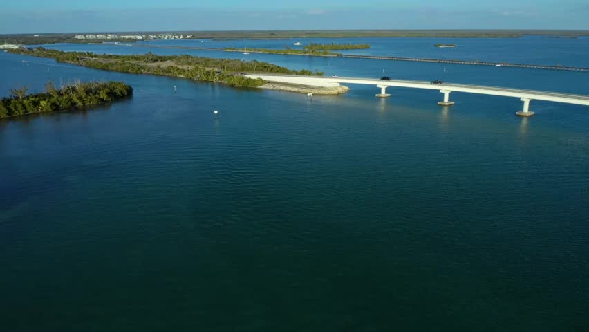 Bridge spanning across a serene water channel with green islands and light traffic, showcasing the coastal landscape and infrastructure in Florida.
