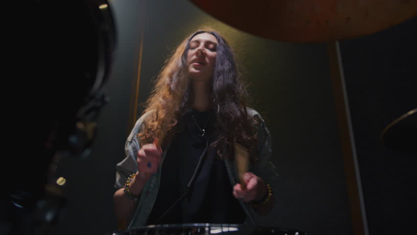 Woman drummer plays a drum kit, drumstick. Female musician beats a rock rhythm on drums, cymbals. Girl artist is rehearsing in a room or performing on festival stage. Alternative indie band in club