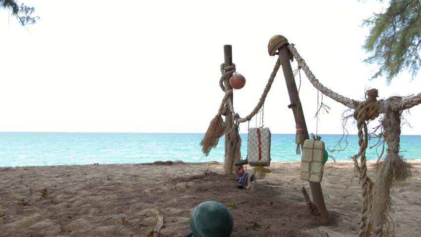 Static wide shot of weathered fishing floats and ropes hanging on a sandy tropical beach
