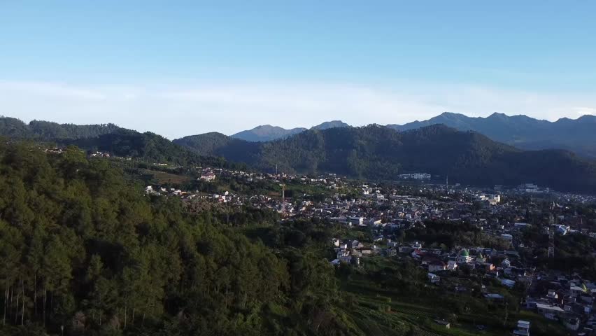 View from the top of the mountain overlooking a rural Indonesian village surrounded by green vegetable farms, winding roads, and fresh mountain air, creating a peaceful countryside landscape.
