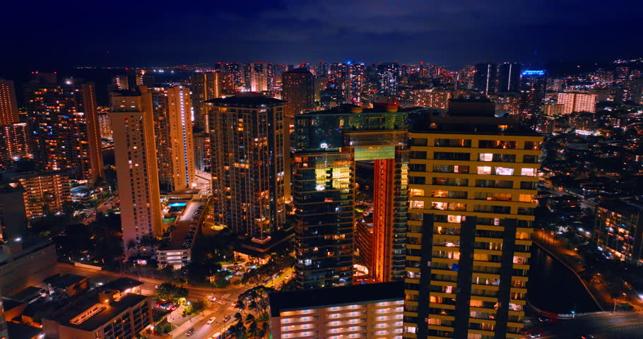 Flight at the tops of high-rise buildings with switched on illumination in the windows. Lively Honolulu, Hawaii, USA at night.