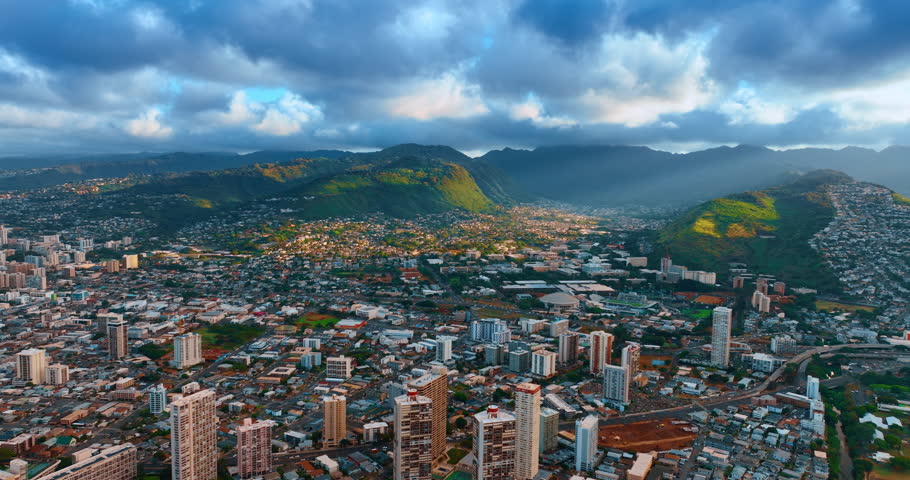 Flying over the residential area of Honolulu, Hawaii, USA. Verdant mountains at backdrop are under the dramatic cloudscape. Aerial view.