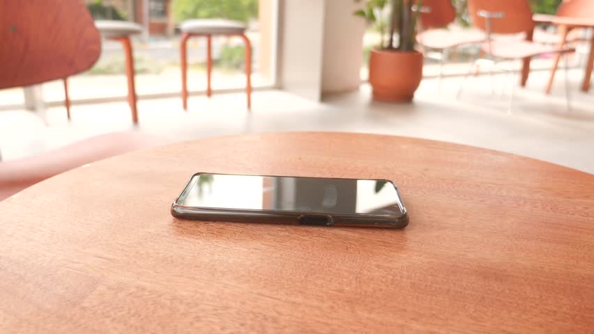 Woman hand picking up smartphone from wooden table in cafe motion