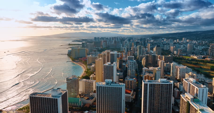 Dramatic clouds cover the sky over the scenery of Honolulu, Hawaii, USA. Slow waves roll to Waikiki shore at sunset. Aerial perspective.