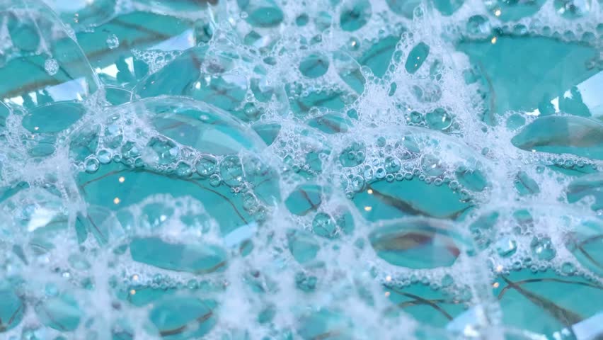 Close-up captures vibrant Blue water with many bubbles and thick foam. Soap suds create abstract pattern, reflecting light for clean, refreshing effect.