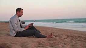 Businessman chatting on tablet computer on the beach
