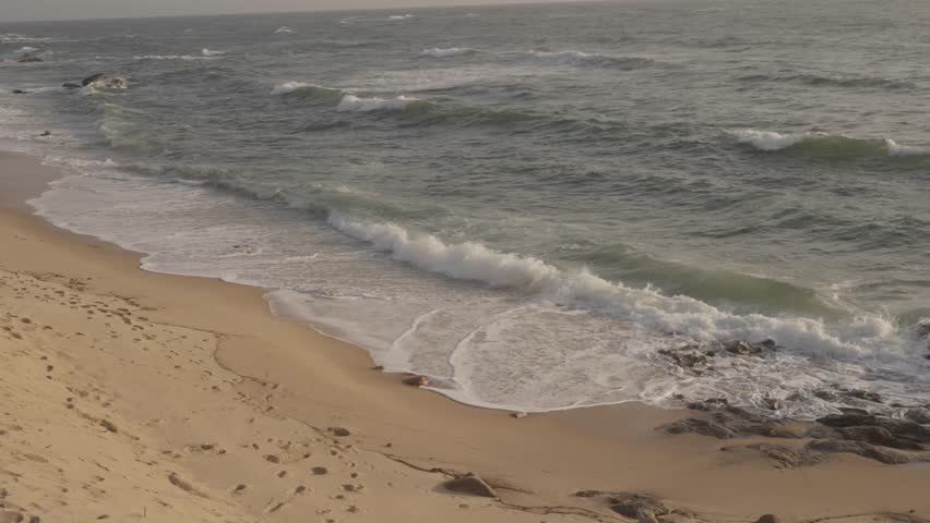 Gentle ocean waves breaking and washing over sandy beach shoreline with rocks