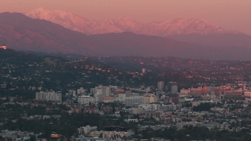 Aerial telephoto dolly shot of Hollywood with snow-covered mountains in the background during magic hour in Los Angeles, California. 4K