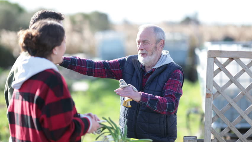 Spouses and mature male neighbor communicate in garden, chat, discuss news, share information. Rustic setting, summer residents gossip next to arched trellis discussing news