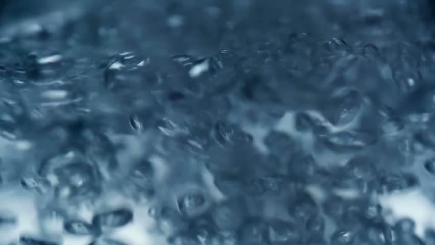 Close-up shot of clear water vigorously boiling, creating numerous ascending bubbles and textural patterns in blue. Liquid is heated and bubbling aggressively.