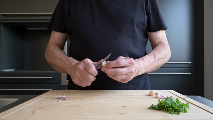 Older man peeling garlic on a wooden cutting board