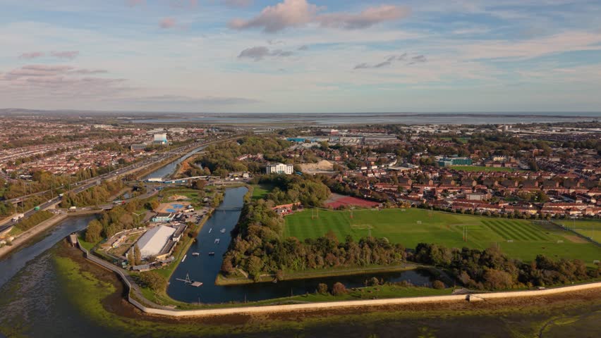 Portsmouth UK flight over commercial and residential areas of the city with waterways and boats, sports field and flying towards harbour and sea on bright sunny day