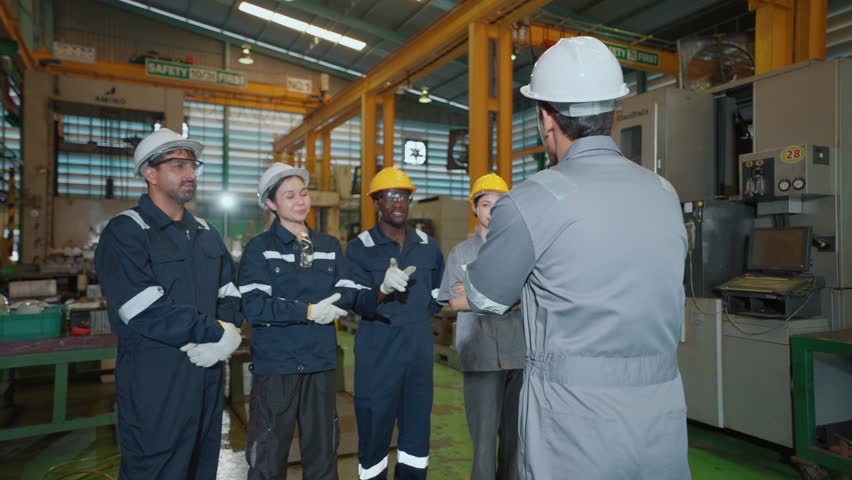 A team leader of multi-ethnic mechanical technicians or engineers explaining work details in a medium-sized automotive parts manufacturing factory, representing a globally standardized quality team