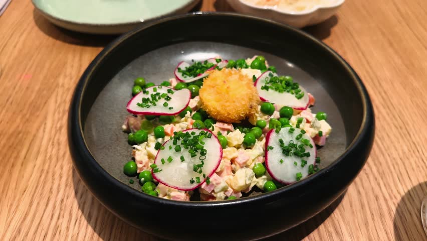 A close-up of Olivier salad on a plate, garnished with radish and egg yolk. High quality 4k footage