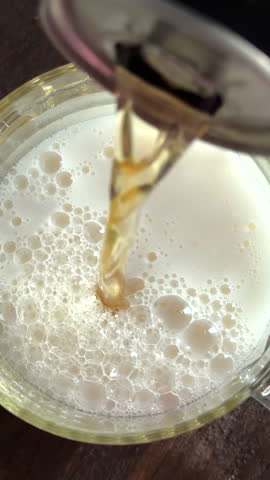 Pouring cold beer from jar in glass, macro. Beer foam close up