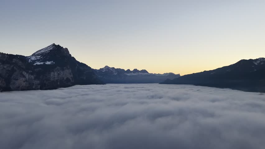 Aerial sunrise above sea of clouds surrounded by dramatic Swiss Alps mountains.