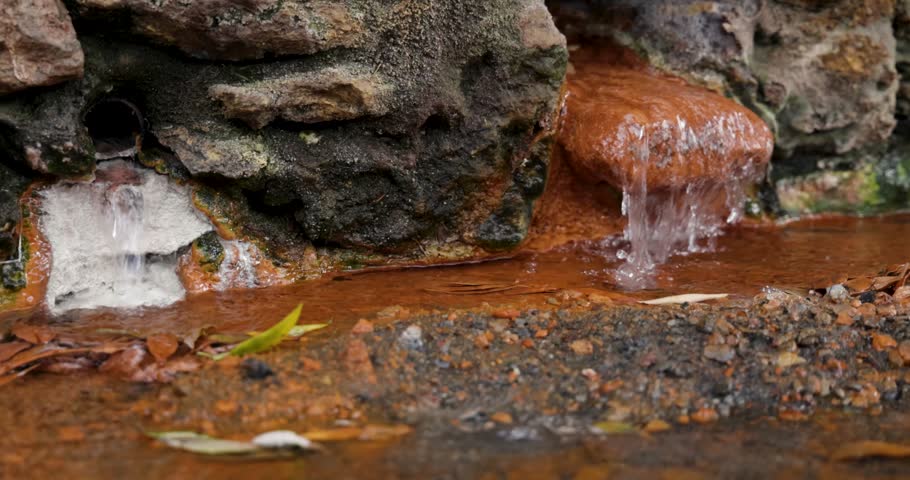 A small stream of water flows through a rocky area. The water is brown and murky, and the rocks are jagged and rough. The scene is peaceful and serene