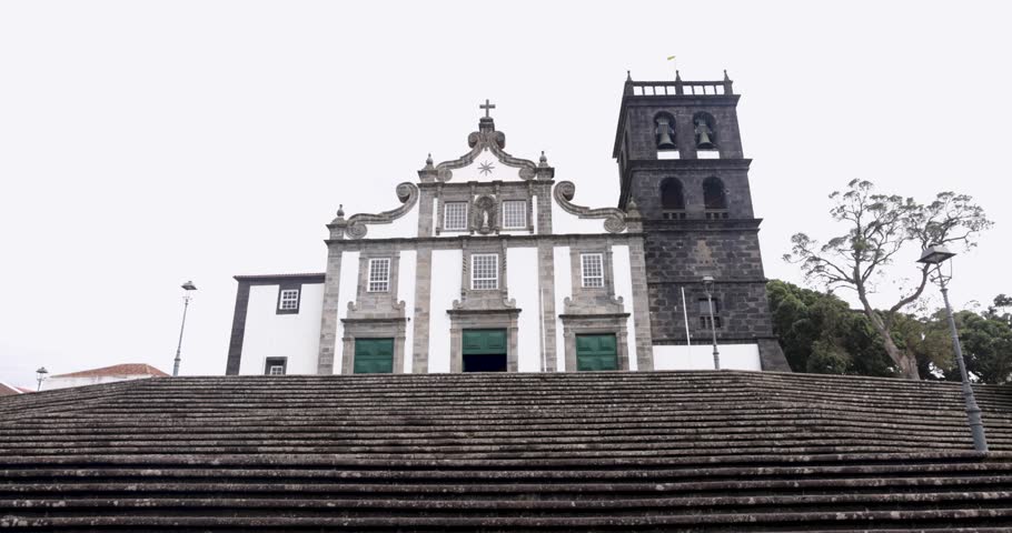 A large church with a steeple and a cross on top in Ribeira Grande, Azores.The building is white and gray