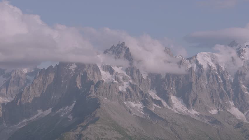 Alpine mountains emerging through clouds under blue sky 