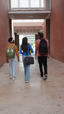 Group of three young multiethnic college students with backpacks and books walking through a modern university building hallway